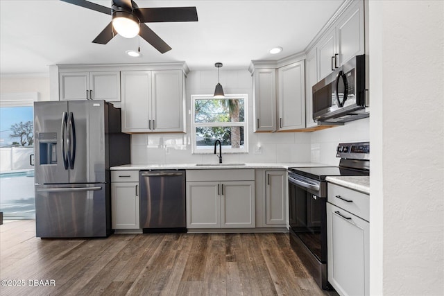 kitchen featuring decorative backsplash, hanging light fixtures, gray cabinets, stainless steel appliances, and a sink