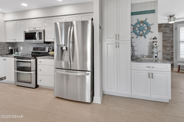 kitchen with appliances with stainless steel finishes, white cabinets, light tile patterned floors, decorative backsplash, and light stone countertops