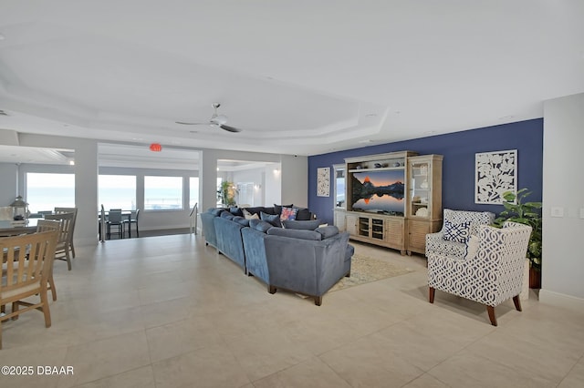 living room with a tray ceiling, light tile patterned floors, a ceiling fan, and baseboards