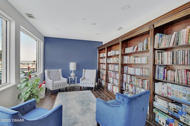 sitting room featuring visible vents, baseboards, wood finish floors, and wall of books