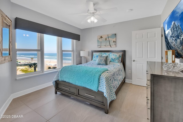 bedroom with a view of the beach, a ceiling fan, baseboards, and a water view