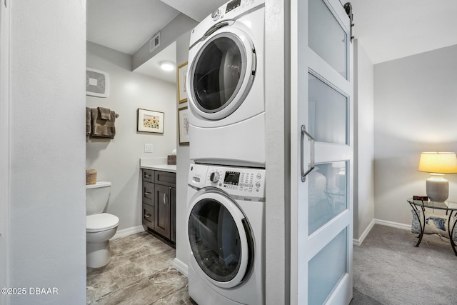 laundry room with laundry area, a barn door, visible vents, baseboards, and stacked washer / drying machine