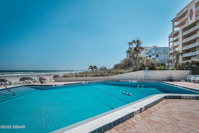 pool featuring a patio area, fence, and a water view