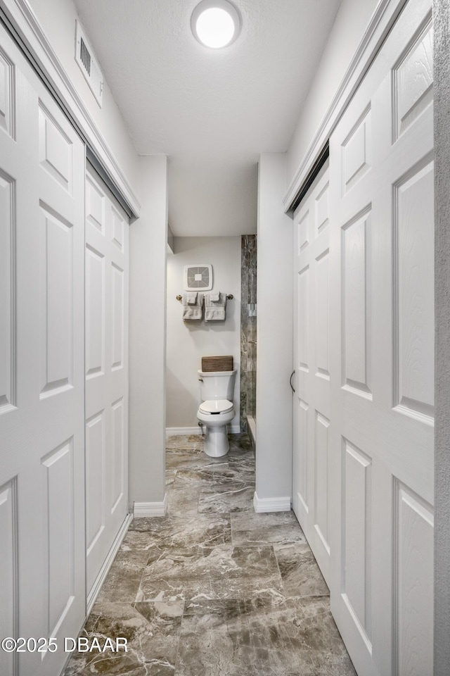 bathroom with toilet, baseboards, visible vents, and walk in shower