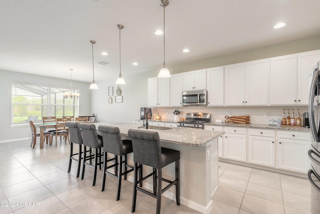 kitchen with stainless steel appliances, pendant lighting, a kitchen island with sink, and light stone counters