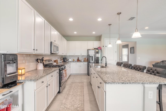 kitchen with stainless steel appliances, a breakfast bar area, white cabinetry, and a kitchen island with sink