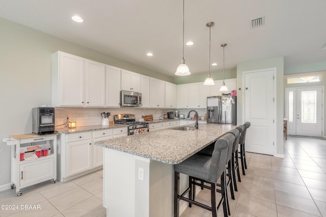 kitchen with stainless steel appliances, light stone countertops, sink, an island with sink, and white cabinets