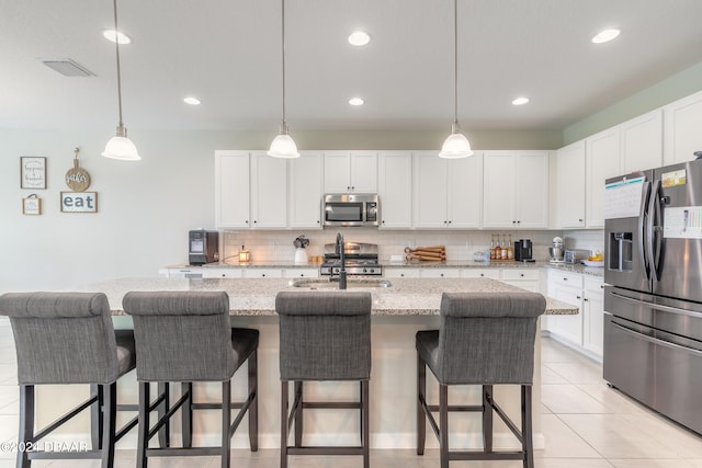 kitchen with white cabinetry, stainless steel appliances, a center island with sink, and light stone counters