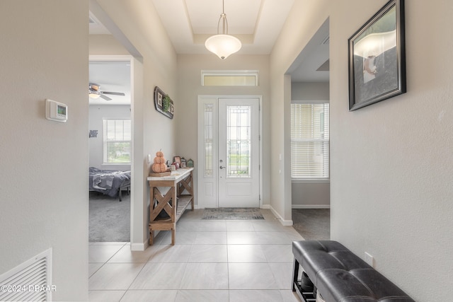 tiled entryway featuring a tray ceiling, ceiling fan, and plenty of natural light