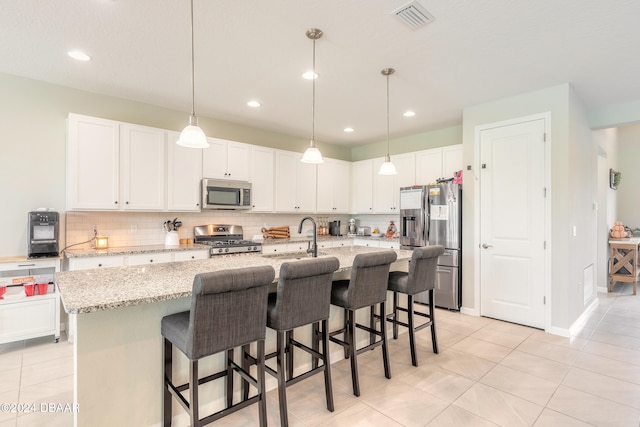 kitchen with stainless steel appliances, light stone countertops, a center island with sink, and white cabinets