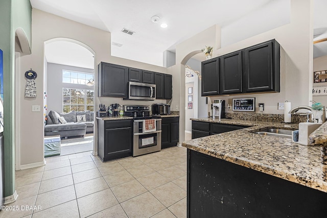 kitchen with light tile patterned floors, appliances with stainless steel finishes, sink, and stone counters