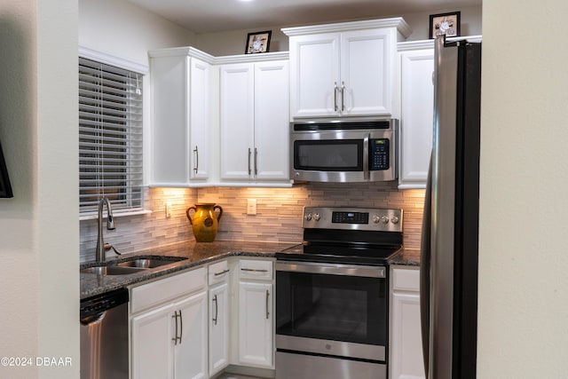 kitchen with tasteful backsplash, dark stone counters, stainless steel appliances, sink, and white cabinetry