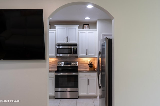 kitchen with backsplash, stainless steel appliances, light tile patterned floors, dark stone countertops, and white cabinets