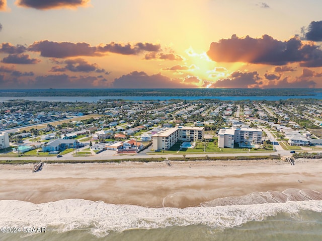 aerial view at dusk featuring a water view and a beach view