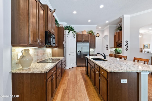 kitchen featuring light stone counters, light hardwood / wood-style floors, black appliances, a kitchen island with sink, and sink