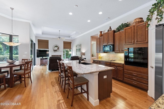 kitchen with sink, pendant lighting, light stone countertops, a center island with sink, and black appliances