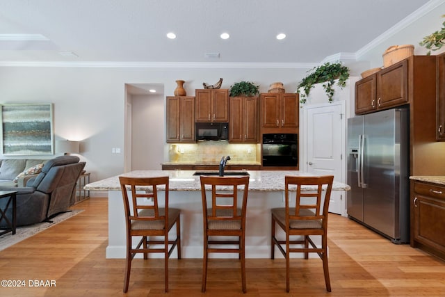 kitchen with light wood-type flooring, an island with sink, black appliances, light stone countertops, and a breakfast bar