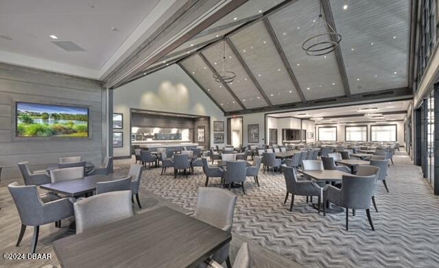 carpeted dining space featuring high vaulted ceiling and beamed ceiling