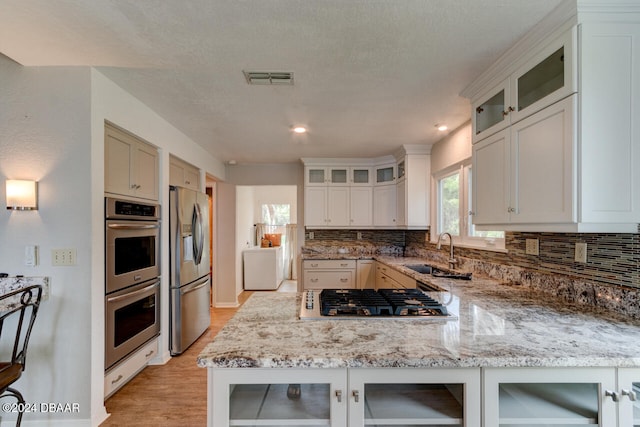 kitchen featuring sink, light hardwood / wood-style flooring, tasteful backsplash, light stone counters, and stainless steel appliances