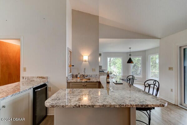 kitchen with lofted ceiling, hanging light fixtures, a kitchen bar, kitchen peninsula, and beverage cooler