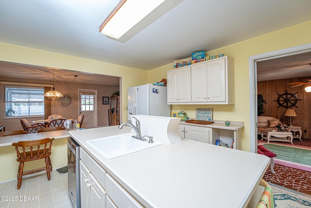 kitchen with white refrigerator with ice dispenser, light countertops, white cabinetry, a sink, and wood walls