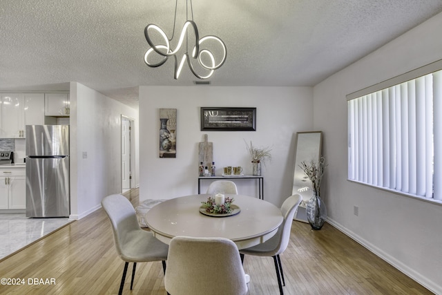 dining space featuring light hardwood / wood-style floors, a textured ceiling, and an inviting chandelier