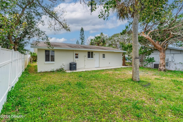 rear view of house featuring stucco siding, a fenced backyard, central AC unit, and a yard