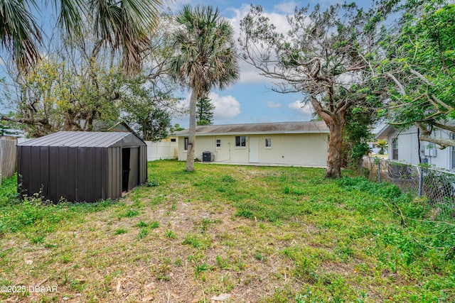 rear view of property featuring an outbuilding, a yard, a storage unit, central AC unit, and a fenced backyard