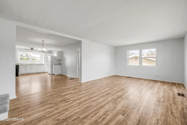 unfurnished living room with baseboards, light wood-style flooring, visible vents, and an inviting chandelier