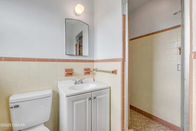 full bath featuring toilet, vanity, tile walls, and wainscoting