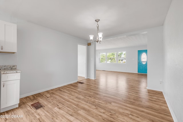 unfurnished dining area featuring an inviting chandelier, light wood-style flooring, visible vents, and baseboards