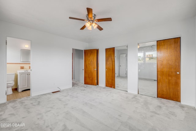 unfurnished bedroom with light carpet, connected bathroom, ceiling fan, multiple closets, and a sink