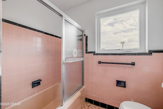 full bath with toilet, bath / shower combo with glass door, wainscoting, and tile walls