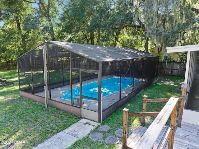 view of pool with a yard, a deck, and glass enclosure