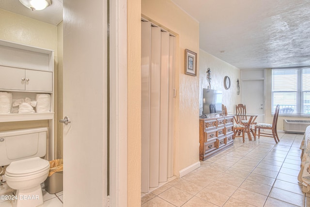 interior space with a wall mounted AC, tile patterned flooring, toilet, and a textured ceiling