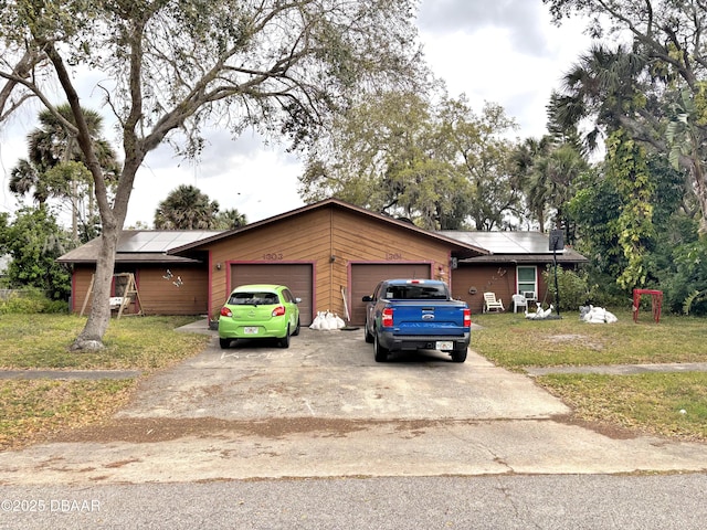 view of front of property featuring solar panels, concrete driveway, a front lawn, and an attached garage