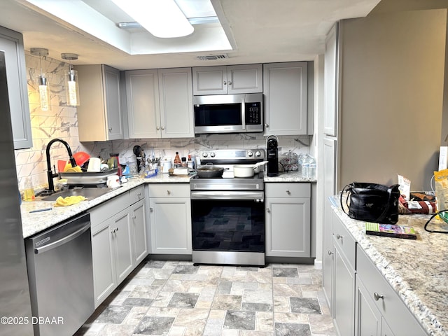 kitchen with stainless steel appliances, gray cabinets, a sink, and tasteful backsplash