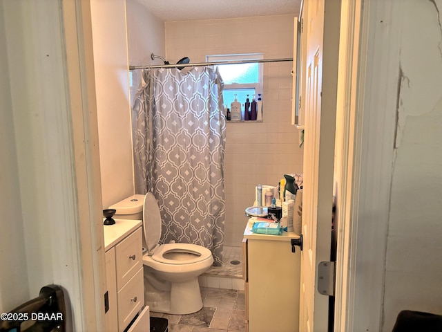 bathroom with stone finish floor, a tile shower, vanity, and toilet