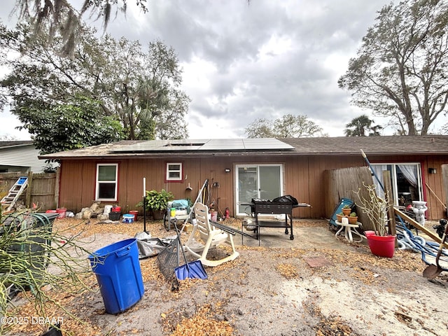 rear view of house featuring roof mounted solar panels, fence, and a patio