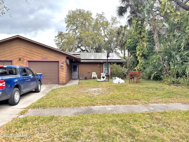 view of front facade with concrete driveway, a front yard, an attached garage, and roof mounted solar panels