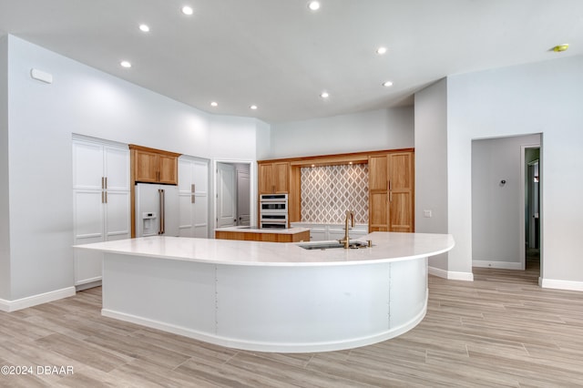 kitchen featuring a large island, a towering ceiling, sink, and white fridge with ice dispenser