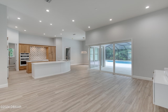 kitchen featuring stainless steel double oven, a large island, decorative backsplash, light hardwood / wood-style floors, and a high ceiling