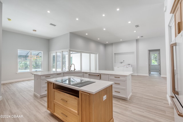 kitchen with black cooktop, white cabinetry, a large island, and light wood-type flooring