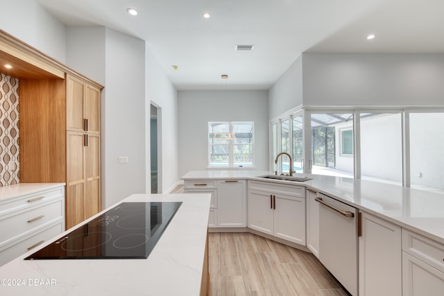 kitchen featuring dishwashing machine, light stone counters, black electric stovetop, sink, and white cabinets