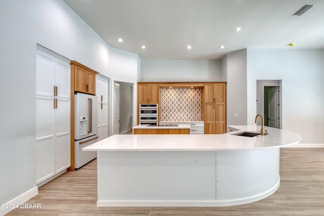 kitchen with sink, light wood-type flooring, high end white refrigerator, and a spacious island