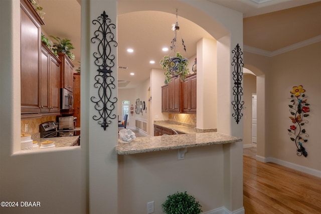 kitchen featuring stainless steel appliances, kitchen peninsula, light stone countertops, light hardwood / wood-style flooring, and crown molding