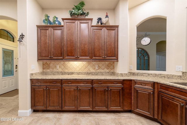 kitchen with light tile patterned flooring, light stone countertops, backsplash, and crown molding