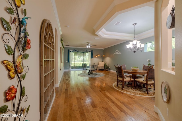 dining space featuring ornamental molding, ceiling fan with notable chandelier, light hardwood / wood-style flooring, and a raised ceiling