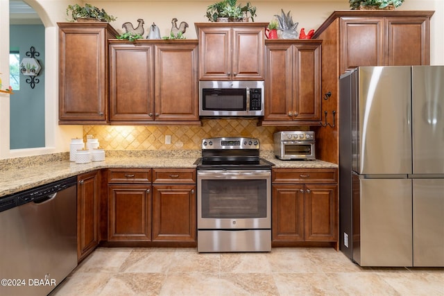 kitchen featuring stainless steel appliances, light stone countertops, and decorative backsplash