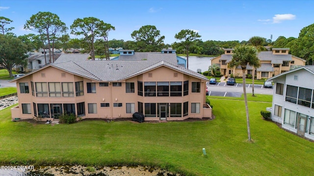 rear view of house with a sunroom, a lawn, and a water view